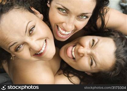 Three nude brunette Caucasian mid-adult women embracing each other looking up at viewer and smiling.