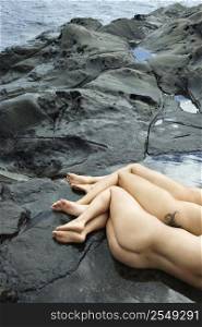 Three nude Caucasian mid-adult women lying side by side on rocky beach in Maui, Hawaii.