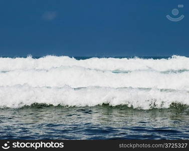 Three ocean waves breaking with clean blue sky in the background