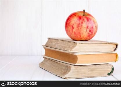 Three old books with red apple on white wooden background