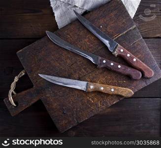 three old kitchen knives on a brown wooden cutting board, top view. three old kitchen knives on a brown wooden cutting board