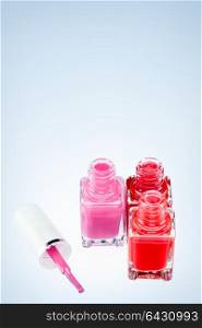 Three open nail polish bottles of different colors on a white surface with one pink brush.