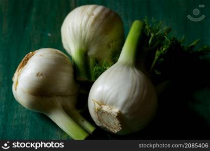Three organic fennel on green wooden background, with imperfections on the peel