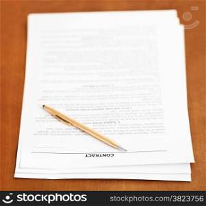 three pages of sales contract and golden pen on wooden table
