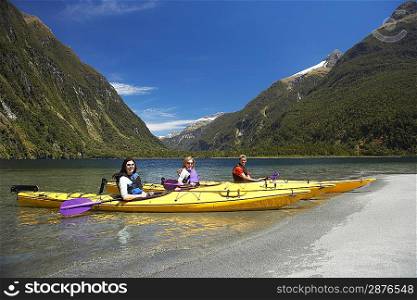 Three people in kayaks at shore of mountain lake