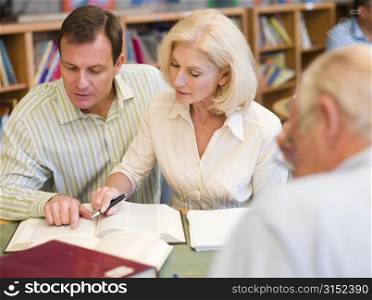 Three people in library with books and notepads (selective focus)