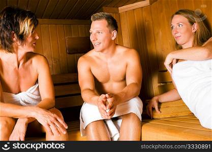 Three people (one male, two female) taking a hot sauna, sitting on various benches