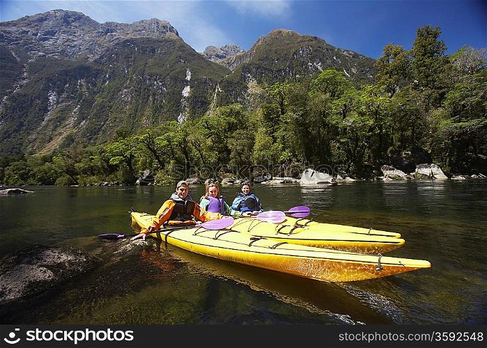 Three people paddling kayaks in mountain lake