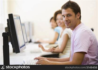 Three people sitting in computer room typing and smiling