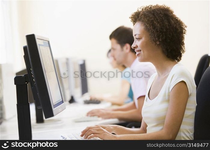 Three people sitting in computer room typing and smiling