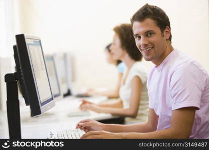 Three people sitting in computer room typing and smiling