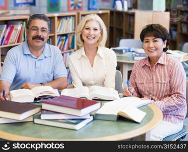 Three people sitting in library with books and notepads (selective focus)