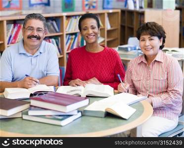 Three people sitting in library with books and notepads (selective focus)