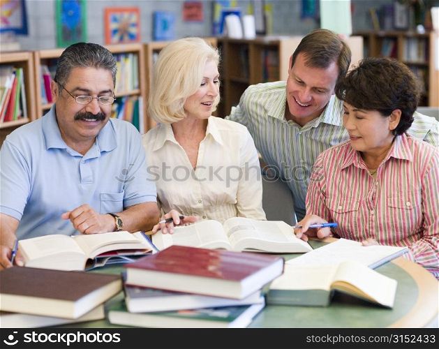 Three people sitting in library with books and notepads while a man leans over them (selective focus)