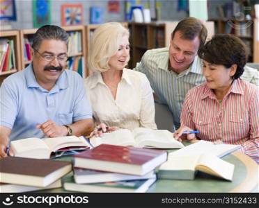 Three people sitting in library with books and notepads while a man leans over them (selective focus)