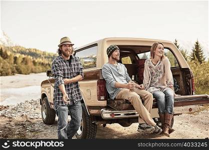 Three people sitting on back of pickup truck smiling