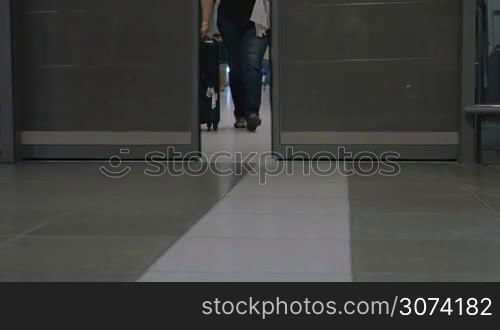 Three people with big roll-on bags walking out of airport terminal through the automatic doors