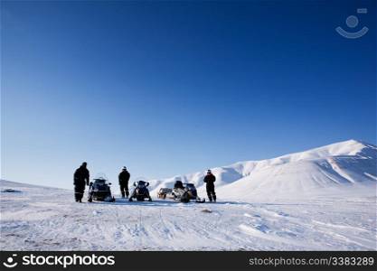 Three people with snowmobiles in an arctic landscape