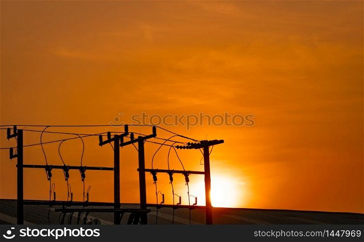 Three-phase electric power for transfer power by electrical grids. High voltage electric poles in factory and roof of building and orange sunset sky. Electric power for support manufacturing industry.