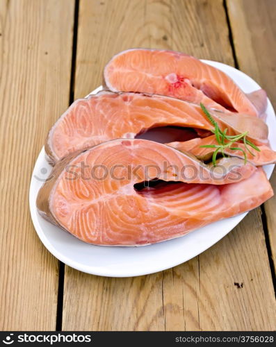 Three pieces of trout in white plate with rosemary on a wooden boards background