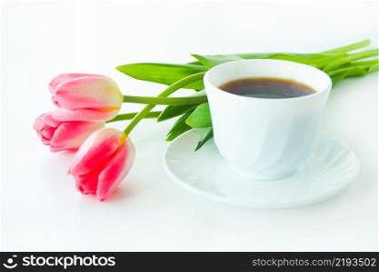 three pink tulips and a cup of coffee on a white table.