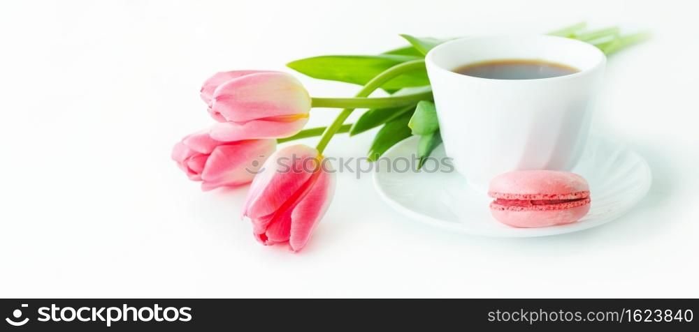 three pink tulips, macarons and a cup of coffee on a white table.