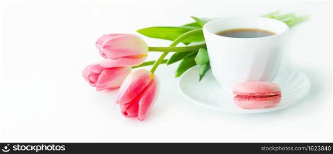 three pink tulips, macarons and a cup of coffee on a white table.
