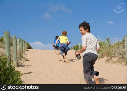 Three pre-teen boys running towards beach
