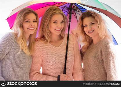 Three pretty young women friends under colorful umbrella parasol. Fashionable females wearing sweaters spending time outdoor.. Three women under colorful umbrella