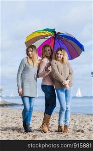 Three pretty young women friends under colorful umbrella parasol. Fashionable females wearing sweaters spending time outdoor.. Three women under colorful umbrella