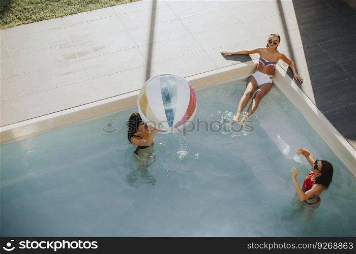 Three pretty young women playing with ball in swimming pool on a summer day