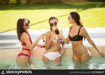 Three pretty young women relaxing and drinking on poolside on a summer day