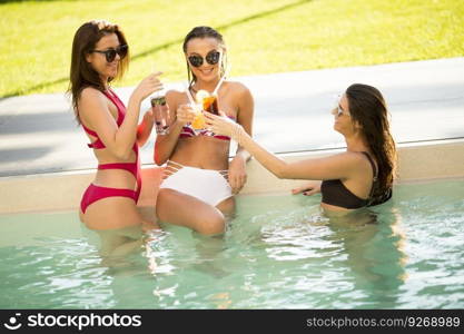 Three pretty young women relaxing and drinking on poolside on a summer day