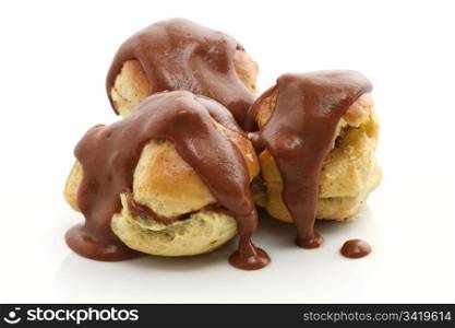 three profiteroles with chocolate sauce over white background