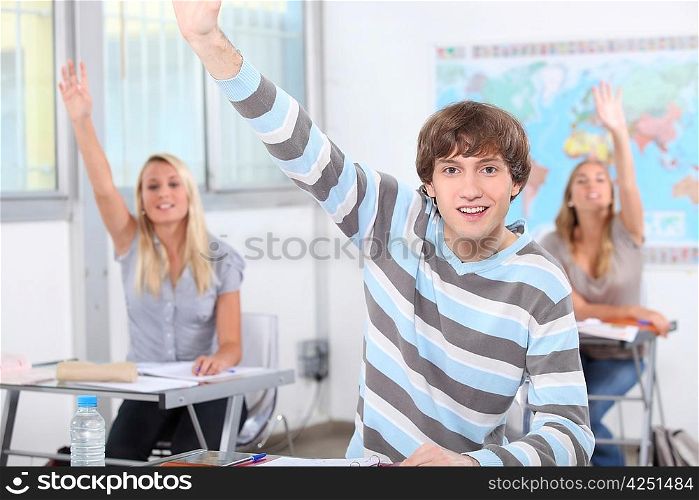 Three pupils in class with arms raised