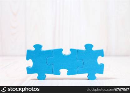Three puzzle pieces on white wooden background. With copy-space for text
