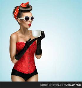 Three-quarter portrait of glamourous pinup girl wearing vintage gloves and red ribbon in her hair, holding a cup of hot coffee or tea and cooling it.