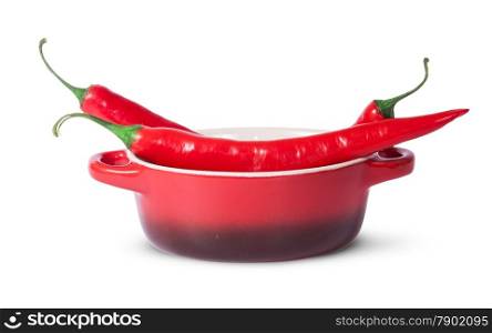 Three red chili peppers in saucepan isolated on white background