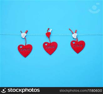 three red felt hearts hanging on a white rope and fastened with a clothespin, blue background. Holiday celebration concept.