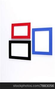Three retro wooden photo frames, red, blue, black on white wall background.
