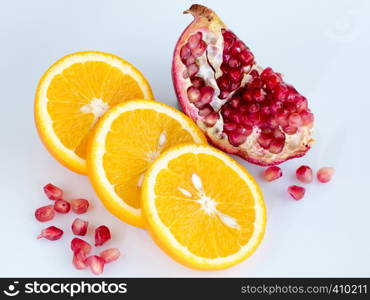 Three rings of sliced juicy ripe orange and a piece of pomegranate with individual grains on a light blue background. Sliced orange and pomegranate on a light blue background