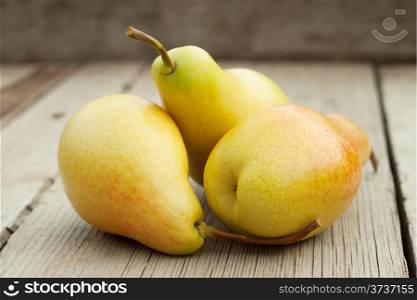Three ripe yellow pears on a wooden background