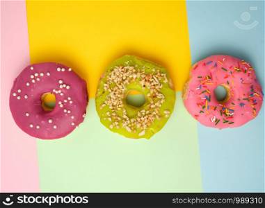three round different sweet donuts with sprinkles on a colored background, pastel colors, top view