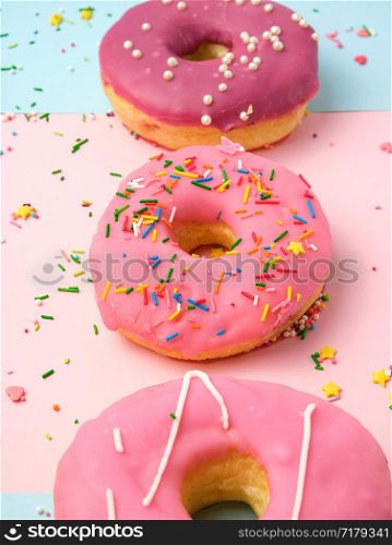 three round different sweet donuts with sprinkles on a pink background, top view, close up
