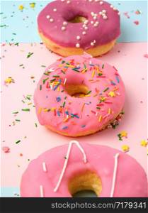 three round different sweet donuts with sprinkles on a pink background, top view, close up