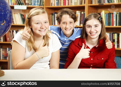 Three school kids in the library, giving thumbs up for education.