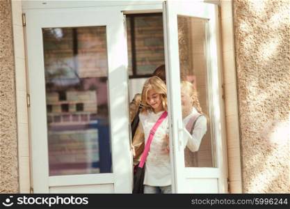 Three schoolgirls entar the door of school building, engoying holidays