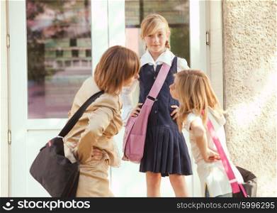 Three schoolgirls outdoors near the door of school building. Three schoolgirls