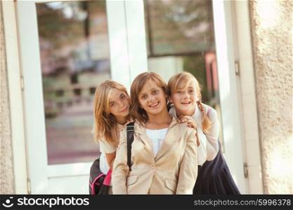 Three schoolgirls outdoors near the door of school building. Three schoolgirls