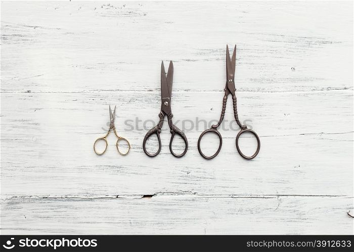 Three scissors on white wooden table